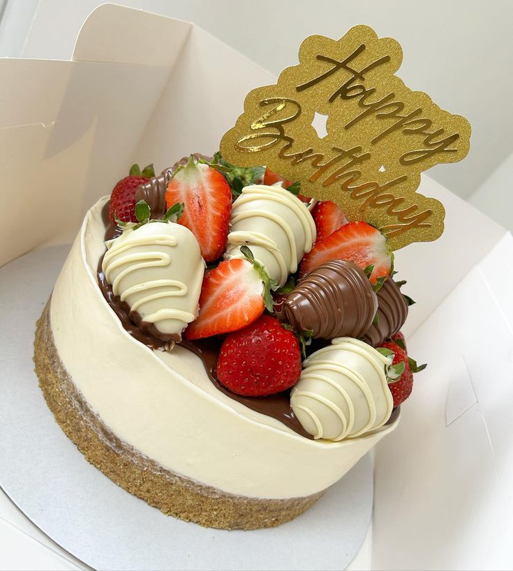 a birthday cake with strawberries and chocolate on top, sitting in a white box