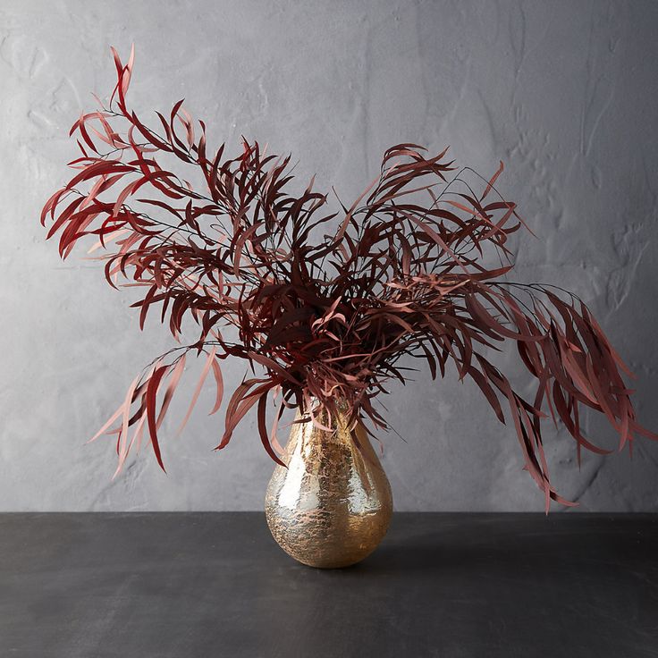 a vase filled with red leaves on top of a table next to a gray wall