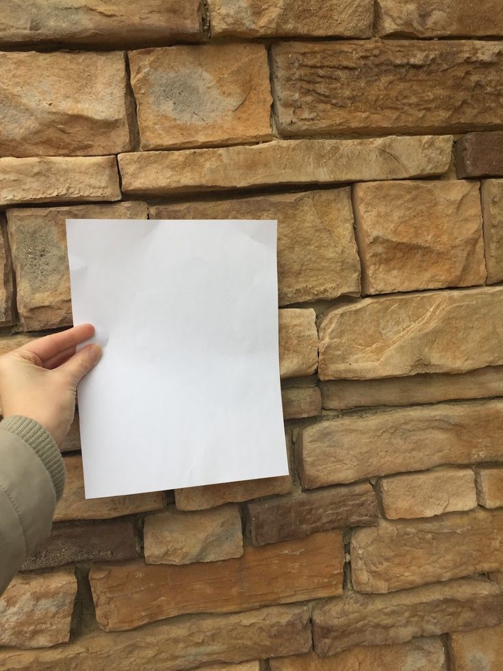 a person holding up a piece of paper in front of a brick wall that is made out of stones