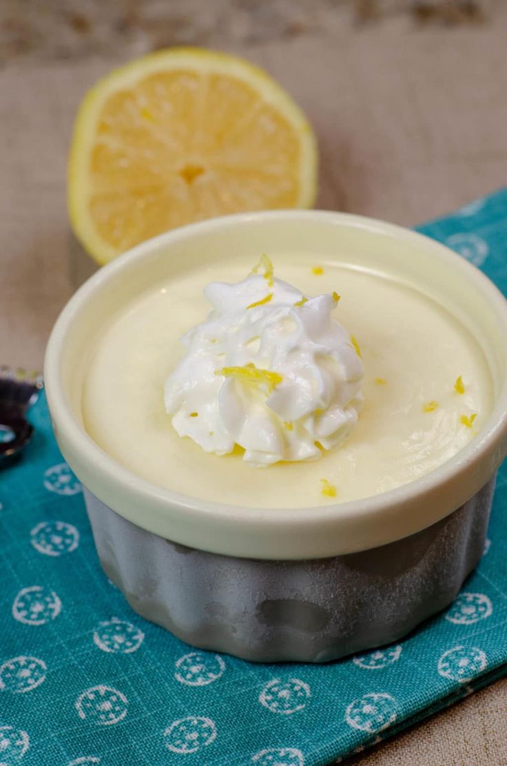 a small bowl filled with whipped cream next to a lemon slice on a blue towel