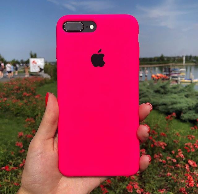 a person holding up a pink iphone case in front of some red flowers and water