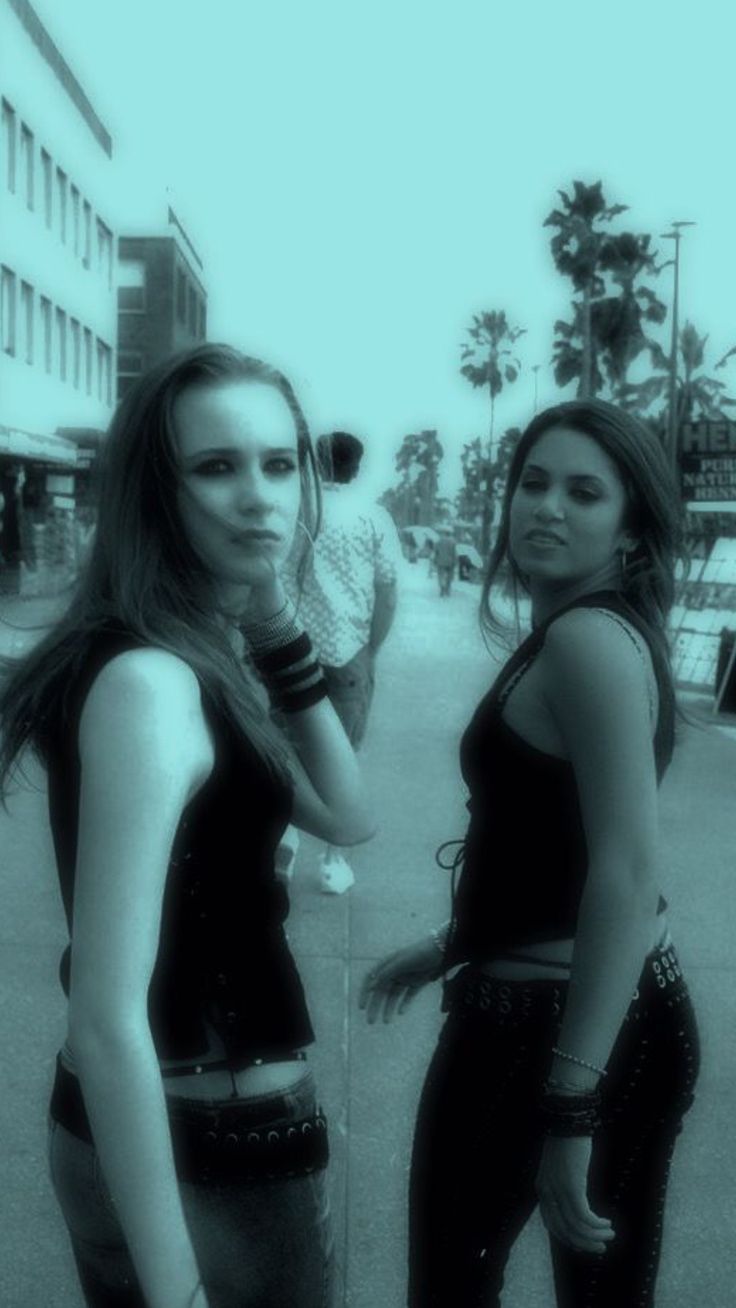 two young women standing next to each other on a city street with palm trees in the background