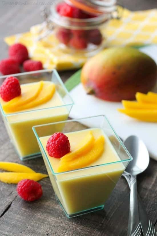 three small glasses filled with fruit on top of a wooden table next to spoons