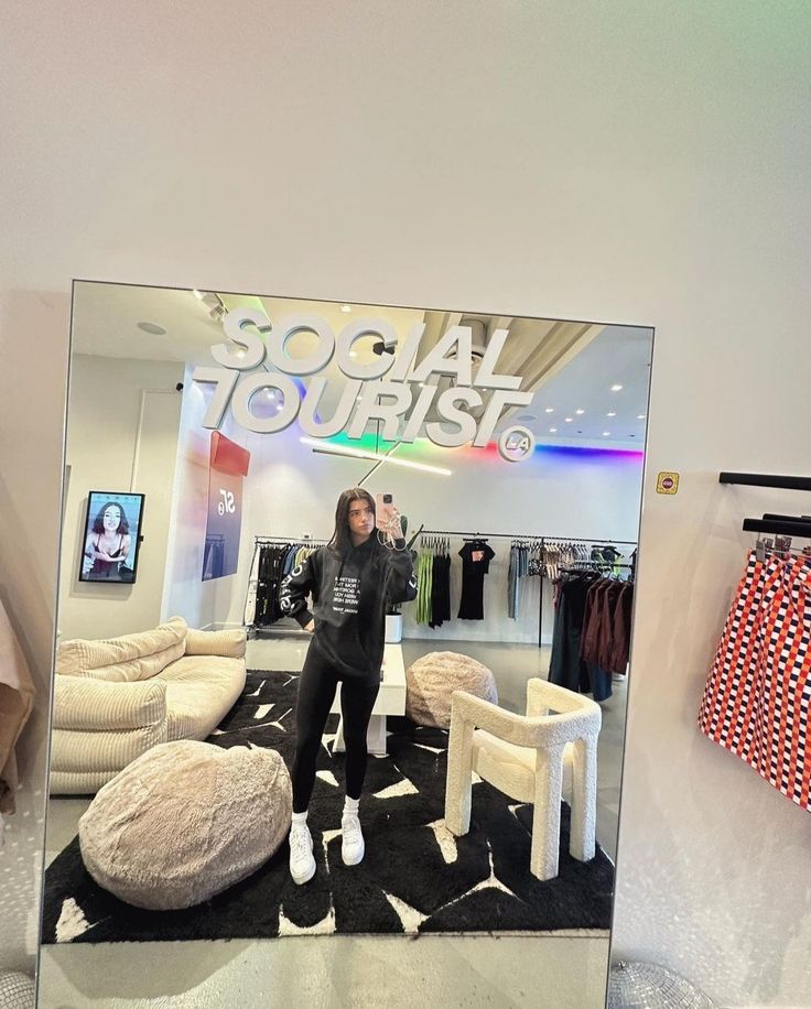 a woman taking a selfie in front of a mirror with clothes hanging on the wall