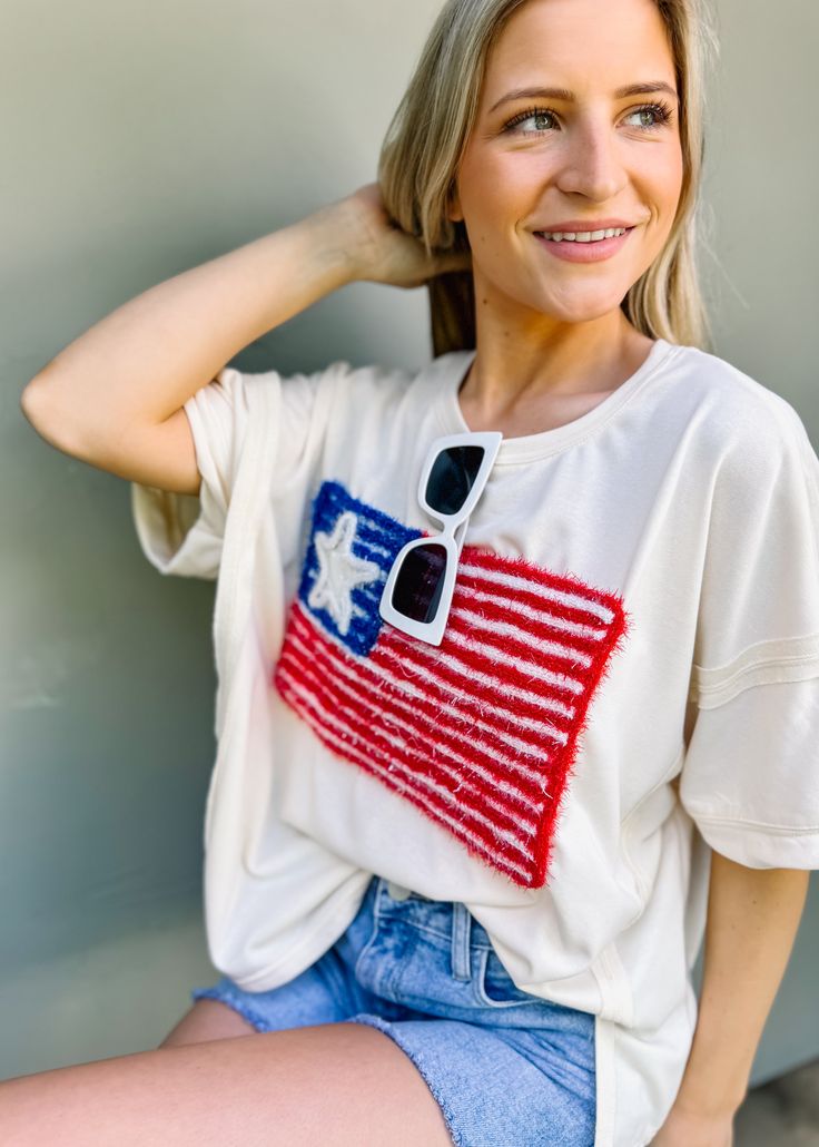 This patriotic tee features a sparkling USA flag embroidery, perfect for Fourth of July celebrations. With a girly and fun touch, it's a must-have for summer outings. Show off your love for America in a unique way with this American Flag Lurex Embroidery Tee. Oversized/ loose fit Round neckline Pull on fit Color: Cream Lurex embroidery Not lined 85% cotton 15% polyester Fabric has little stretch Summer Cotton T-shirt With Star Patch, Trendy Summer T-shirt With Star Patch, Cotton T-shirt With Star Patch For Summer, White Summer T-shirt With Star Patch, Trendy Summer Tops With Flag Print, Summer Flag Print Crew Neck T-shirt, Summer Crew Neck T-shirt With Flag Print, Patriotic T-shirt For Memorial Day, Spring Cotton Tops With Star Patch