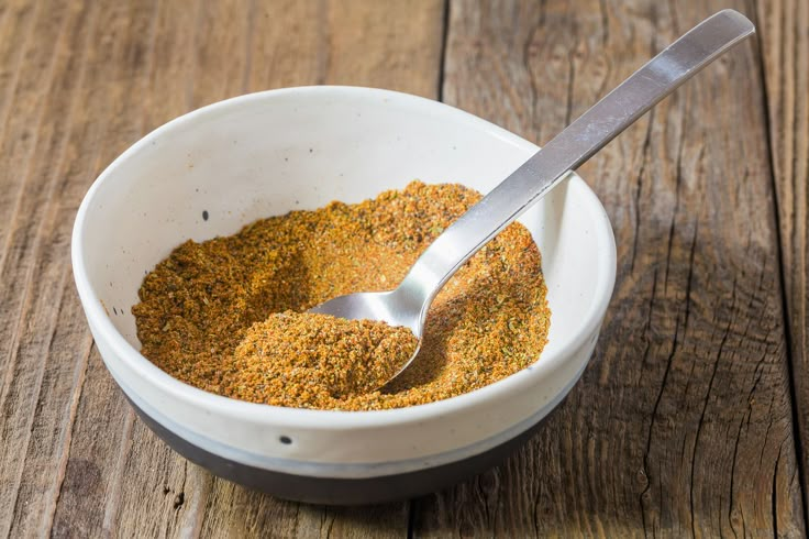 a white bowl filled with spices on top of a wooden table next to a spoon