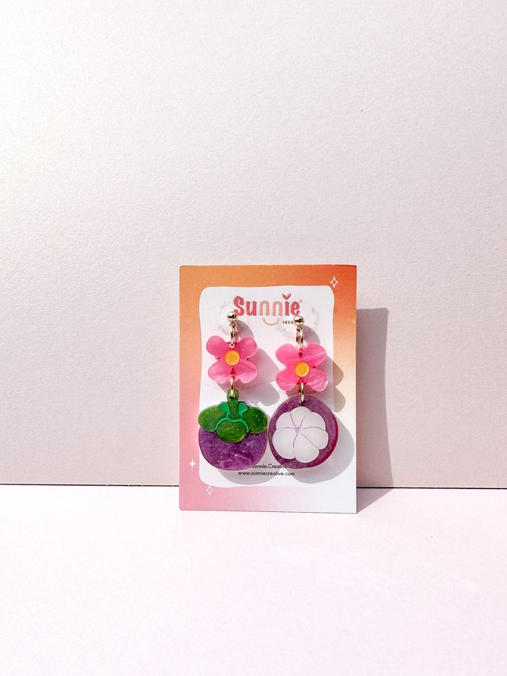 a pair of earrings with flowers on them sitting in front of a white background and an orange card