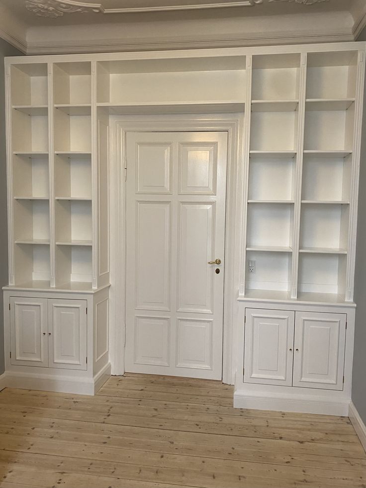 an empty room with white bookcases and wood flooring in front of the door