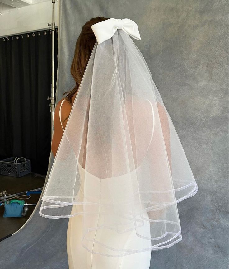 the back of a woman wearing a white wedding veil with a bow on her head