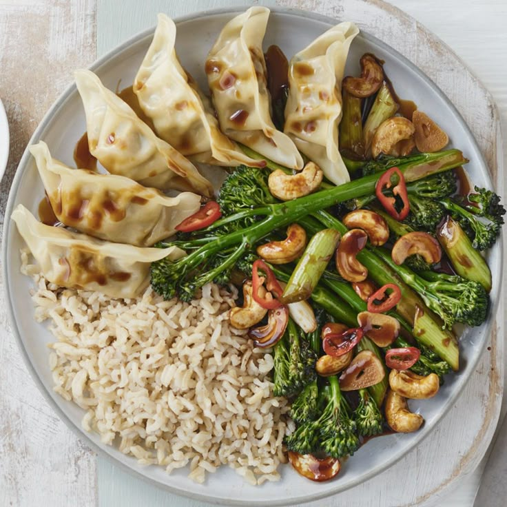 a white plate topped with dumplings and broccoli covered in sauce next to rice