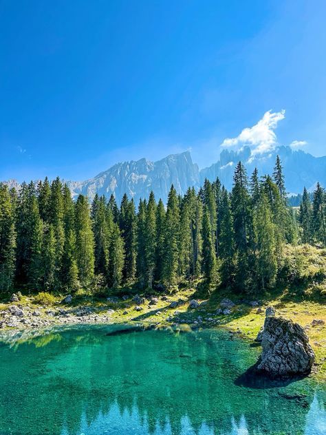 a lake surrounded by trees and mountains with blue water in the foreground on a sunny day