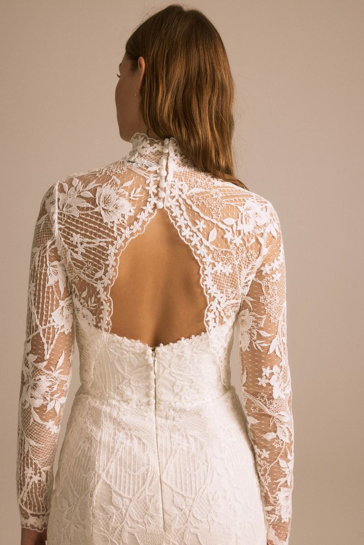 the back of a woman wearing a white wedding dress with sheer lace and open shoulders