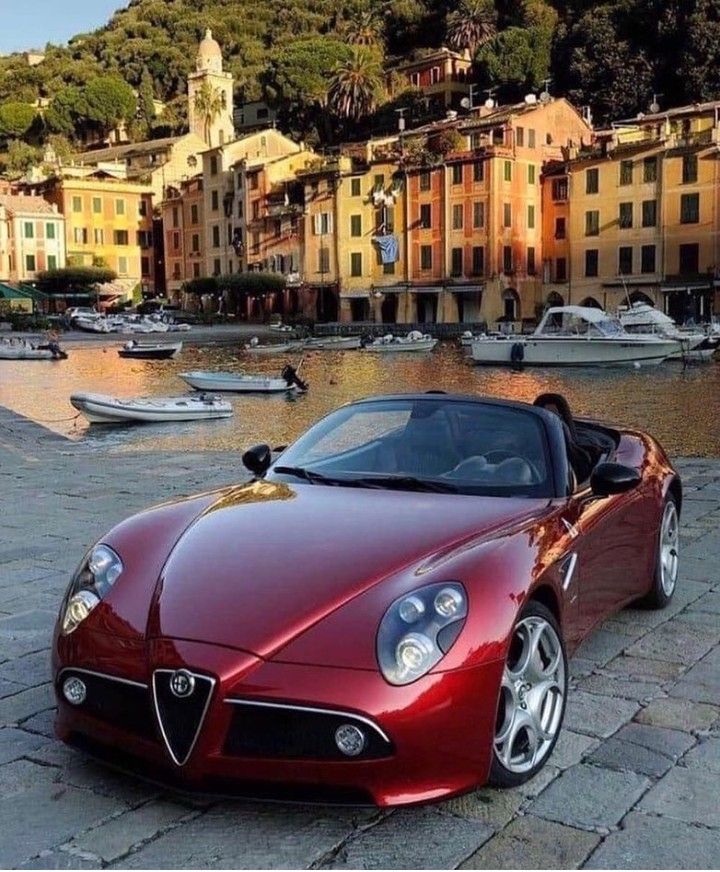 a red sports car is parked in front of some buildings and boats on the water