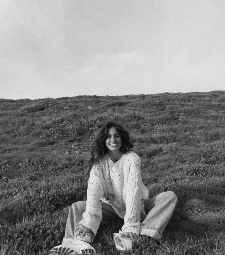 a black and white photo of a woman sitting in the grass on top of a hill