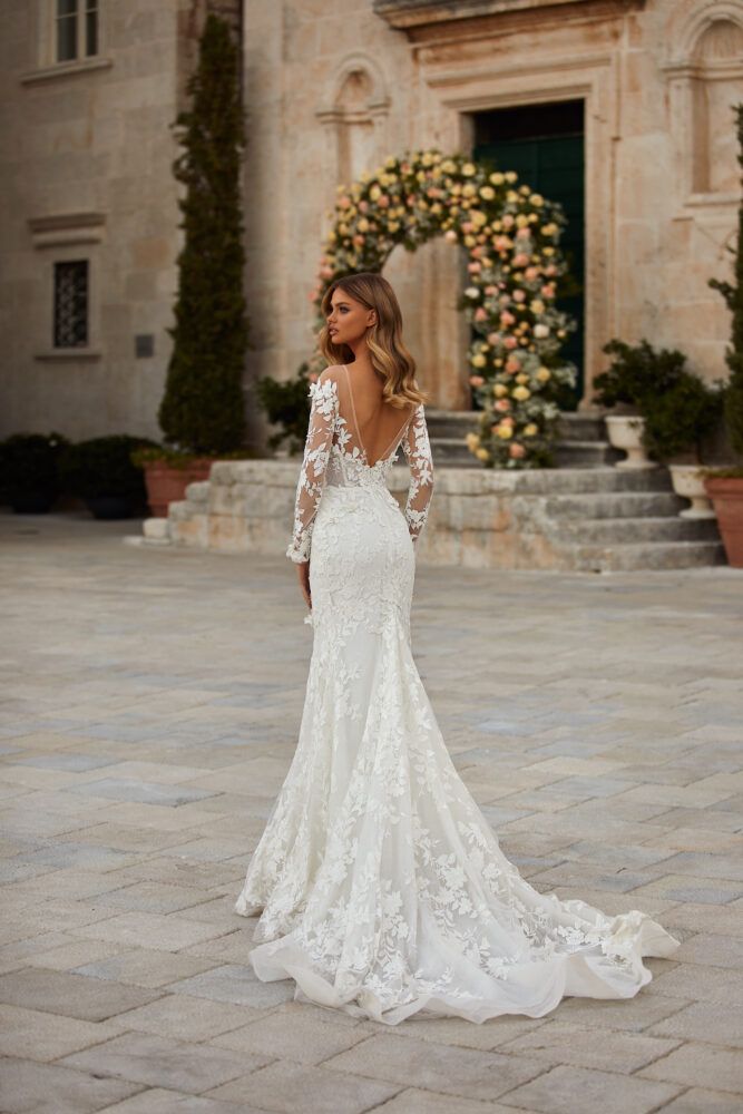 a woman in a white wedding dress standing on a stone walkway with her back to the camera