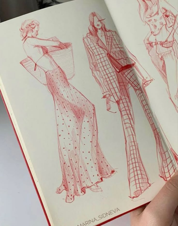 a hand holding an open book with sketches of women's clothing on the pages