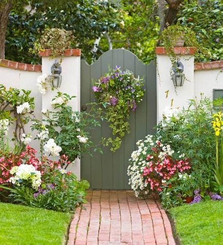 a garden with flowers and plants growing on the side of it, next to a brick path