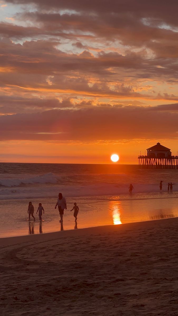 people are walking on the beach at sunset