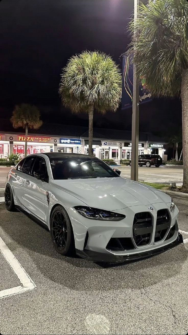 a white sports car parked in a parking lot next to some palm trees at night