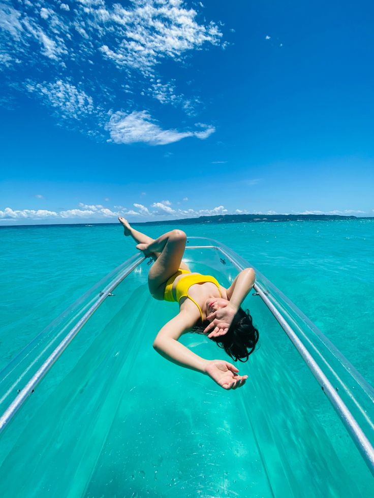 a woman in yellow swimsuit laying on the back of a boat with clear blue water