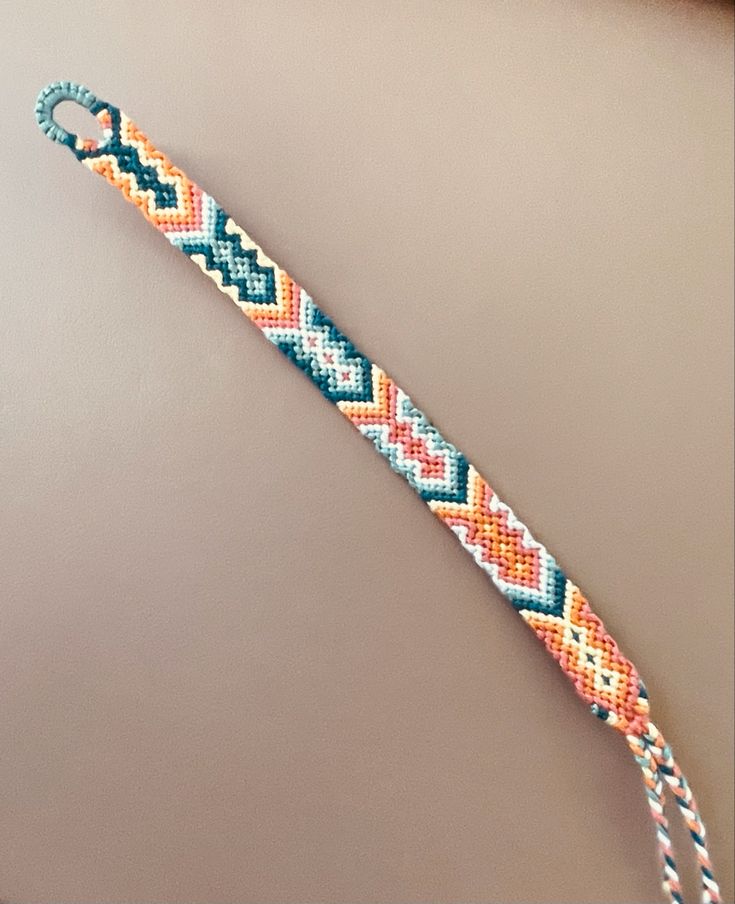 a close up of a beaded bracelet on a white surface with an orange, yellow and blue design