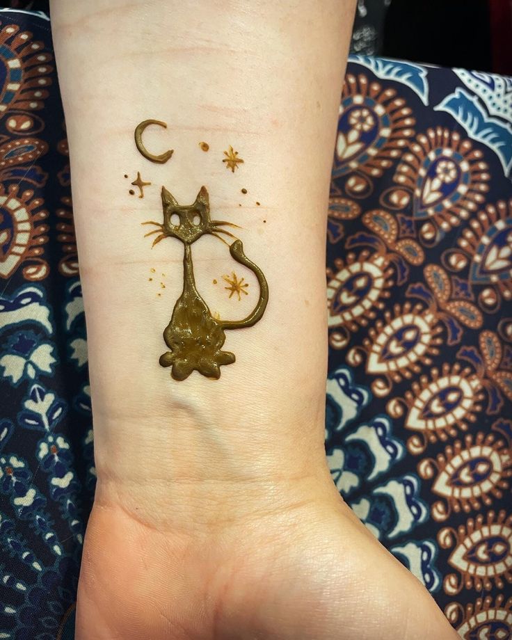 a small tattoo on the wrist of a person with a cat and moon in it