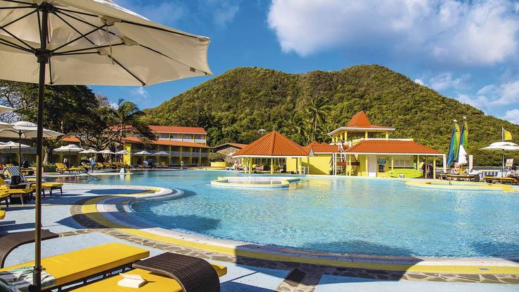 an outdoor swimming pool surrounded by lounge chairs and umbrellas with mountains in the background