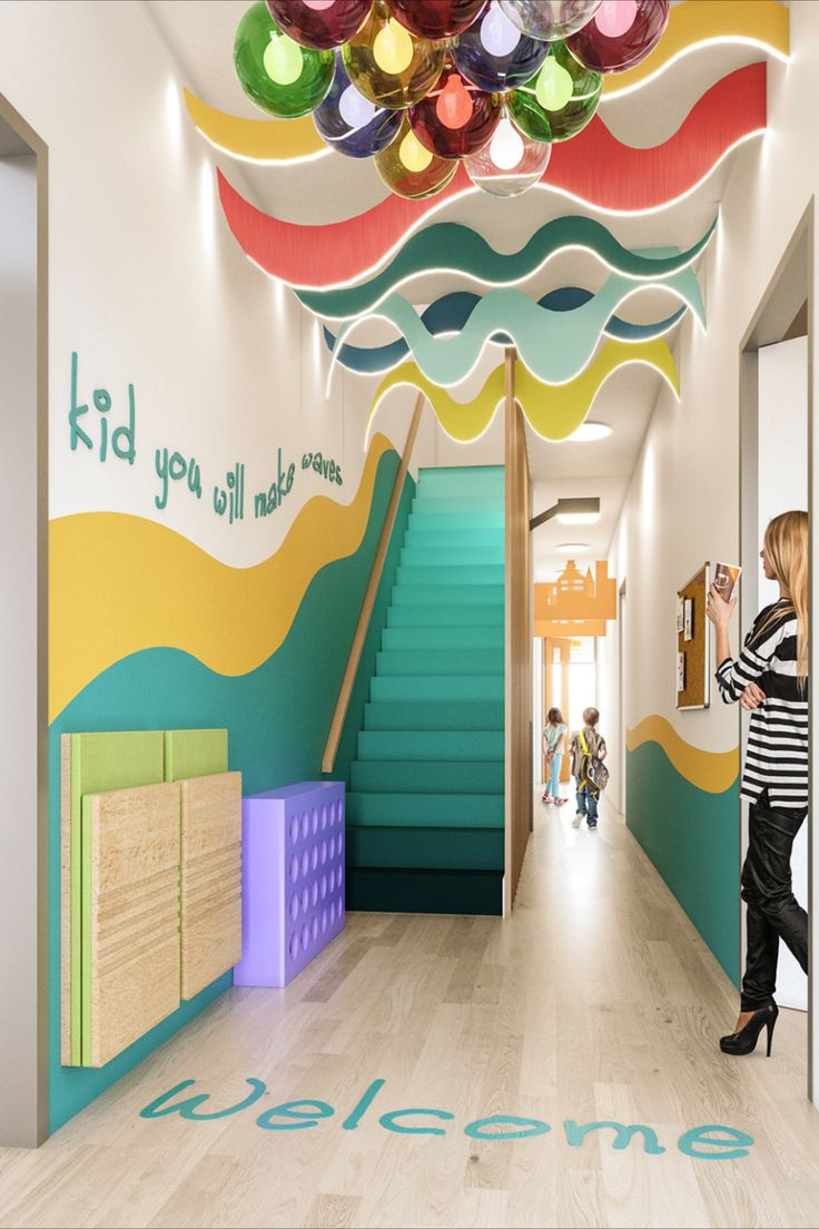 Statement wave effect ceiling and colourful ball lights with an Ombre effect staircase in turquoise. Kids you will make waves in a 3D font along the wall Kindergarten Design Interior, Daycare Entrance, School Wall Design, Kindergarten Interior Design, Kindergarten Entrance, School Reception, Kindergarten Interior, Preschool Designs, Daycare Design