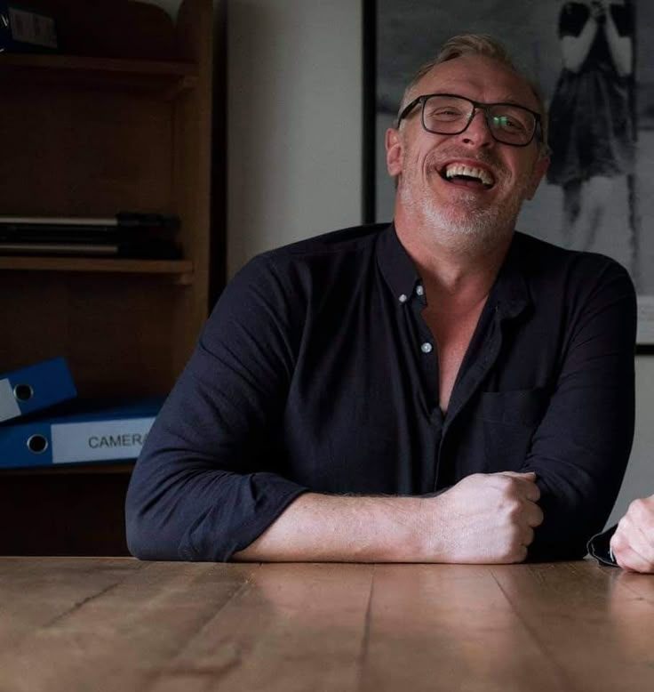 a man sitting at a table with his arms crossed and smiling in front of him