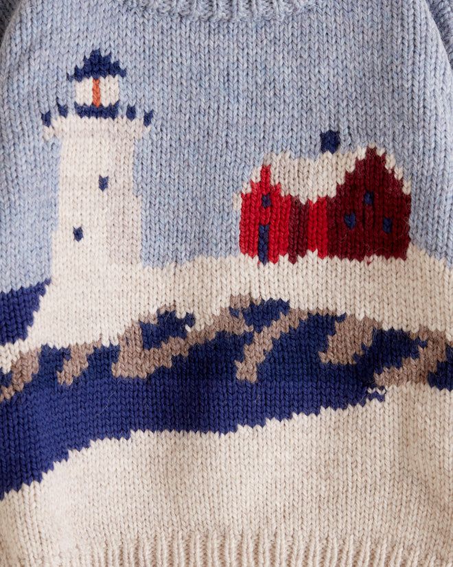 a sweater with a lighthouse on it is shown in blue and white, as well as red