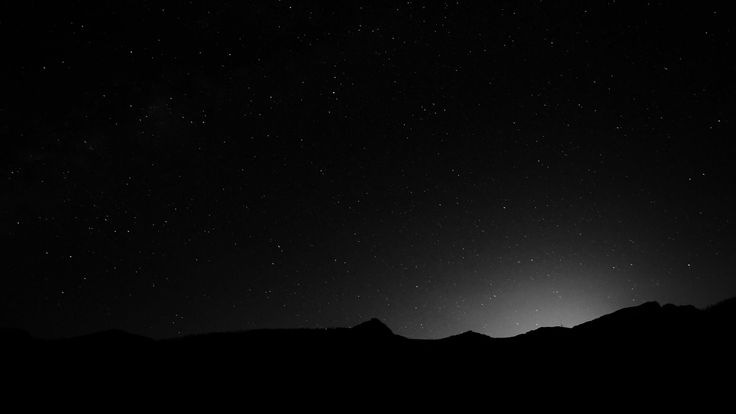 the night sky is full of stars and some dark hills are silhouetted against it