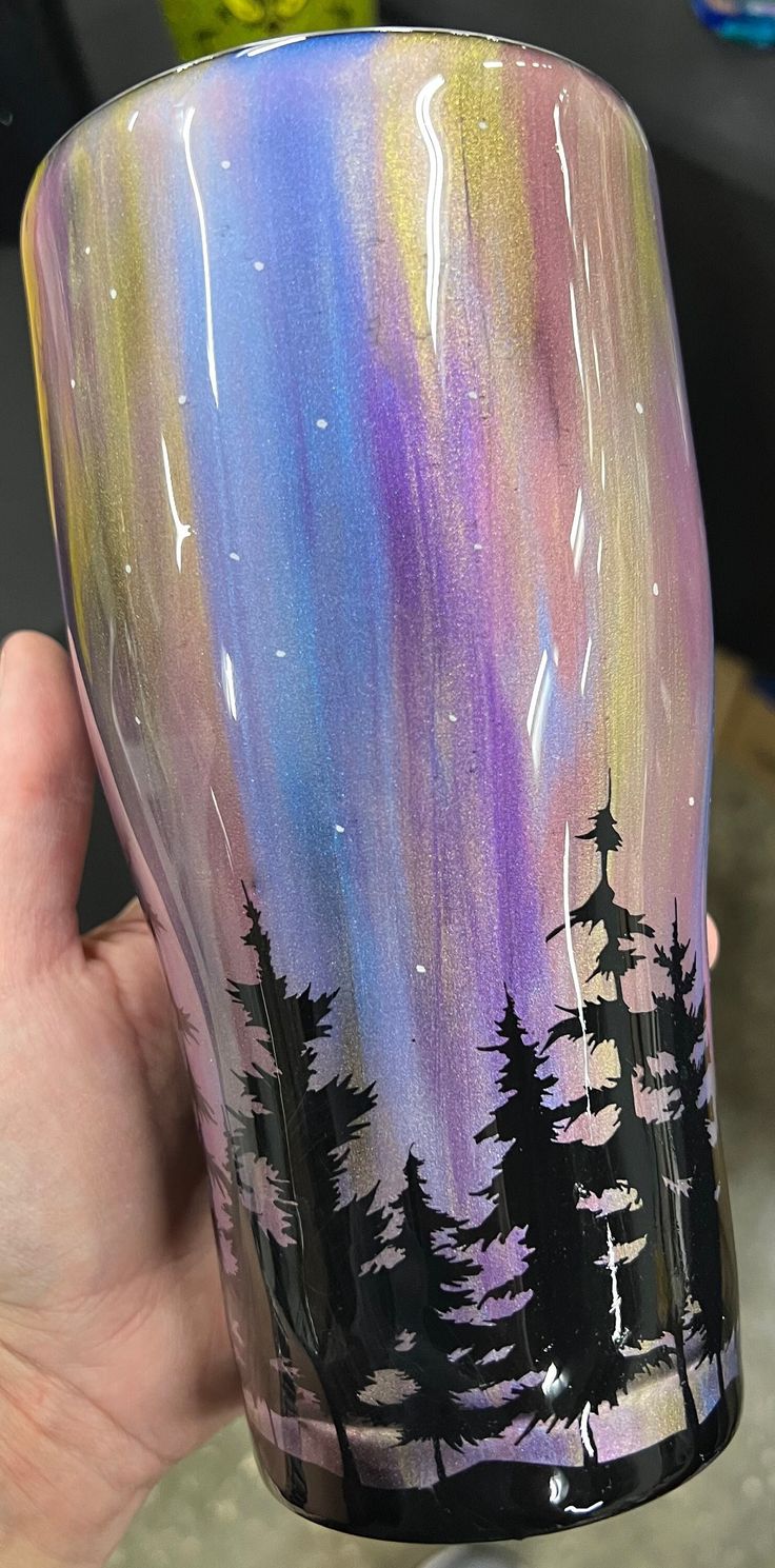 a hand holding up a painted glass with trees on the outside and stars in the sky