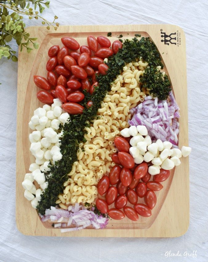 a wooden cutting board topped with pasta and veggies on top of a white table