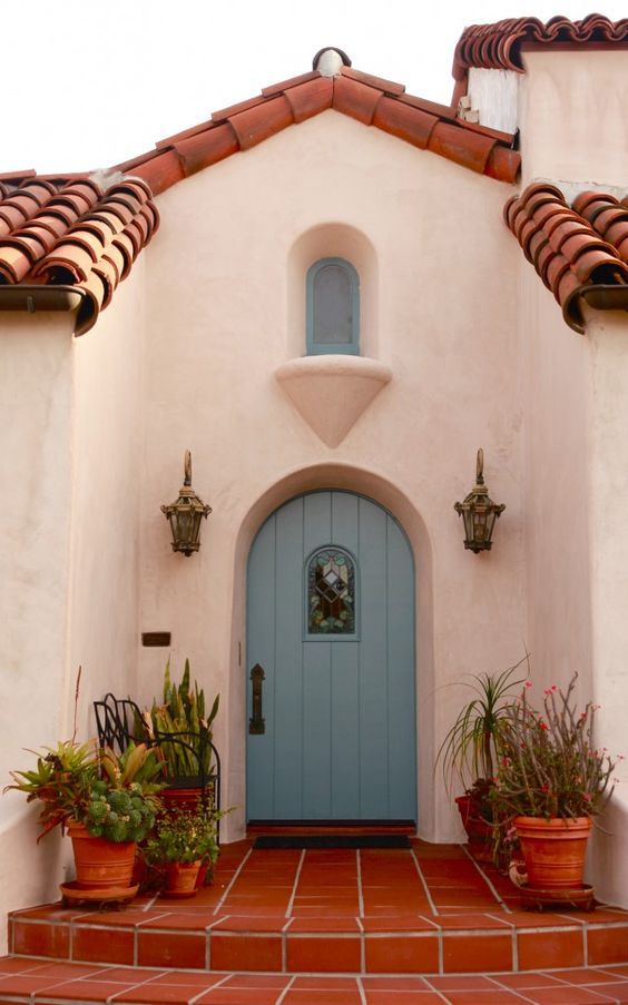 a blue door is on the side of a white stucco building with potted plants