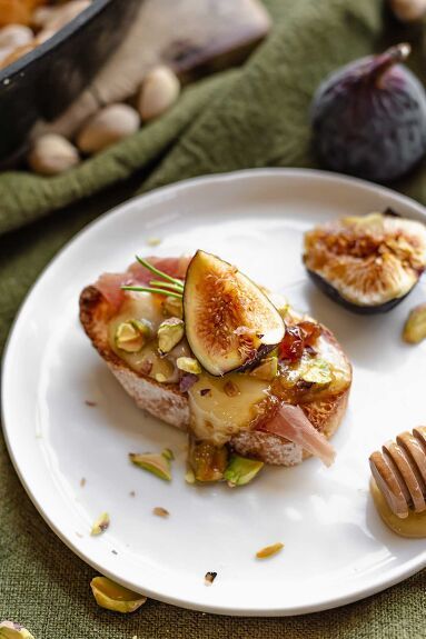 an open faced sandwich with figs, nuts and honey on a plate next to some bread