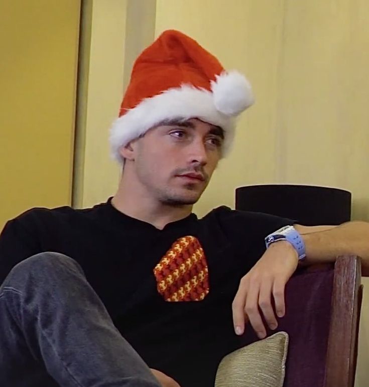 a man wearing a santa hat sitting in a chair with his hand on his hip