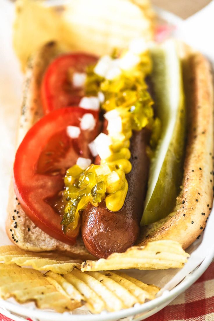 a hot dog with toppings and chips on a plate