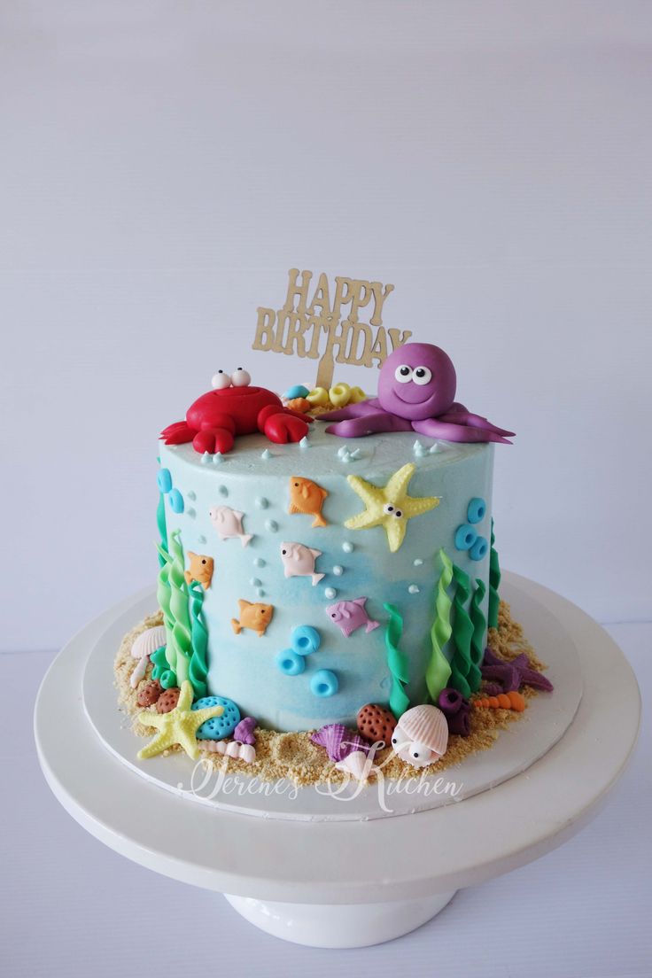 a birthday cake with blue frosting and sea creatures on top, sitting on a white pedestal