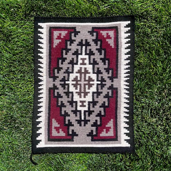 a red and white rug sitting on top of green grass