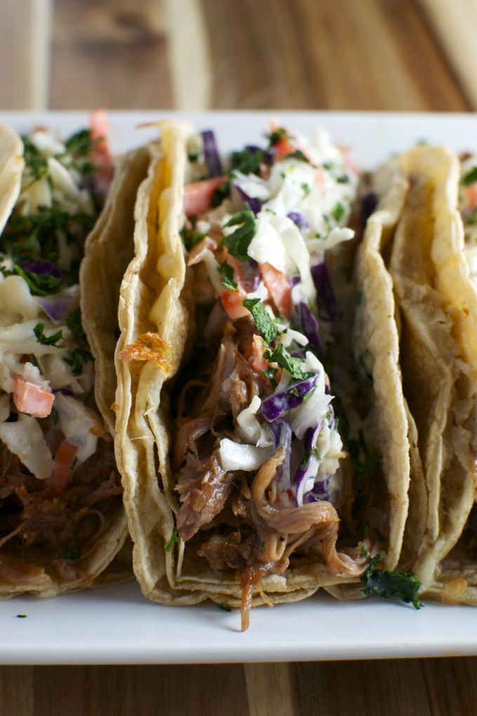 three tacos on a plate with cole slaw and shredded meat in the middle