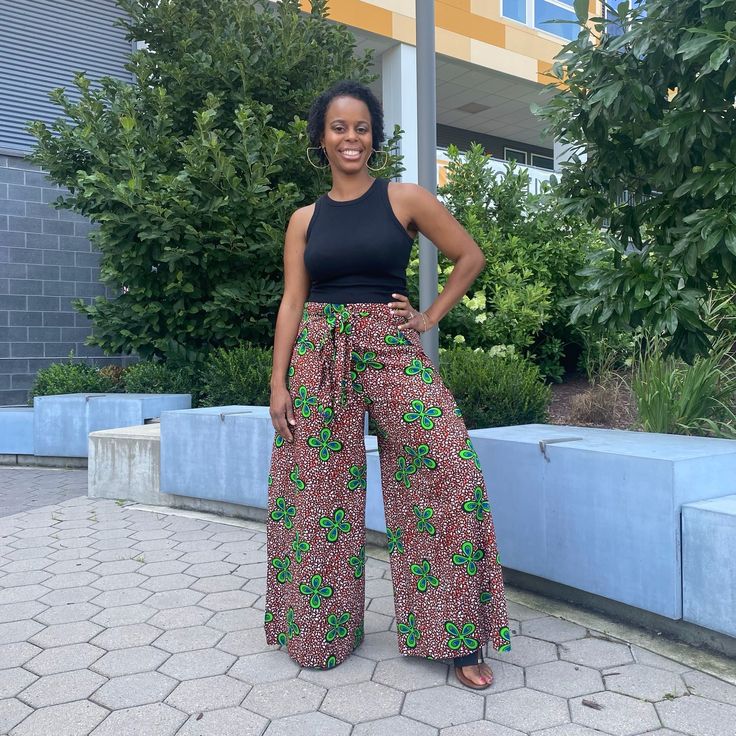 a woman standing in front of a building wearing wide legged pants and black tank top