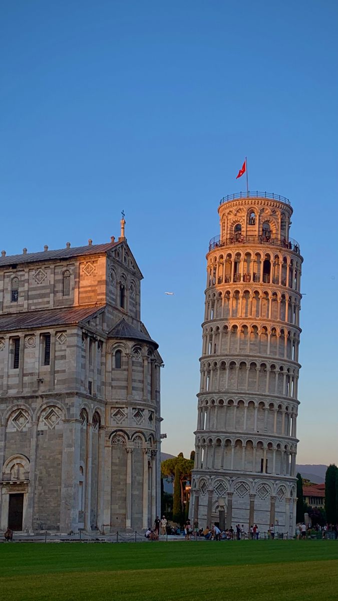 the leaning tower of pisa is shown in front of an old building with a flag on top