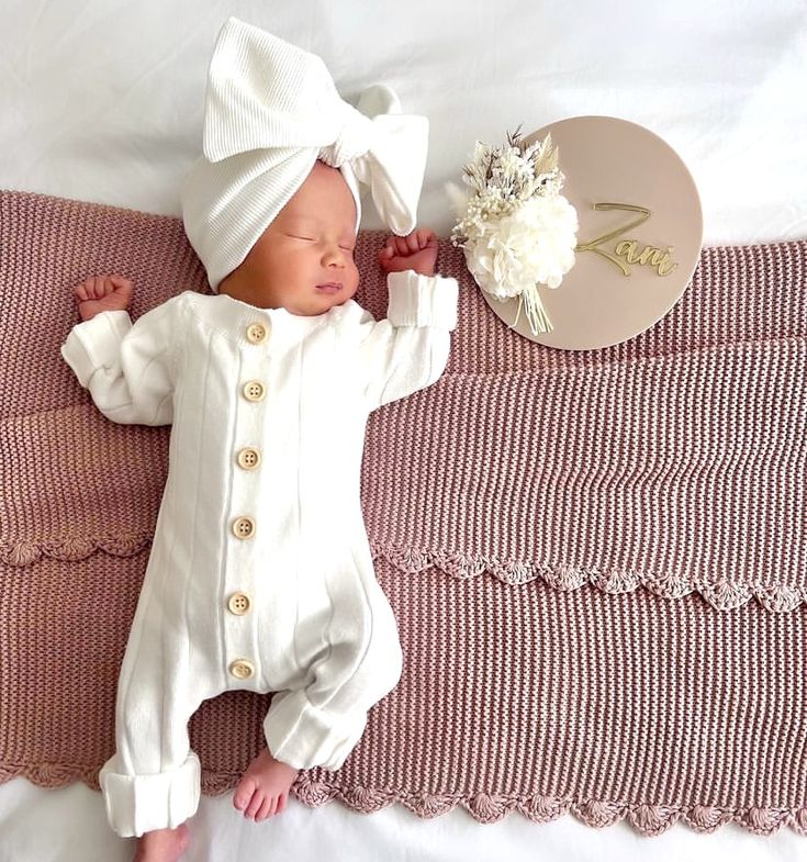 a baby laying on top of a pink blanket next to a white hat and flower