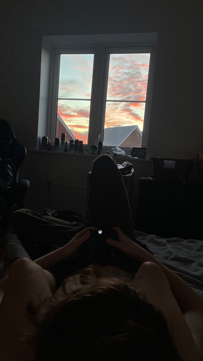 a person laying in bed looking out the window at the sun going down over the mountains