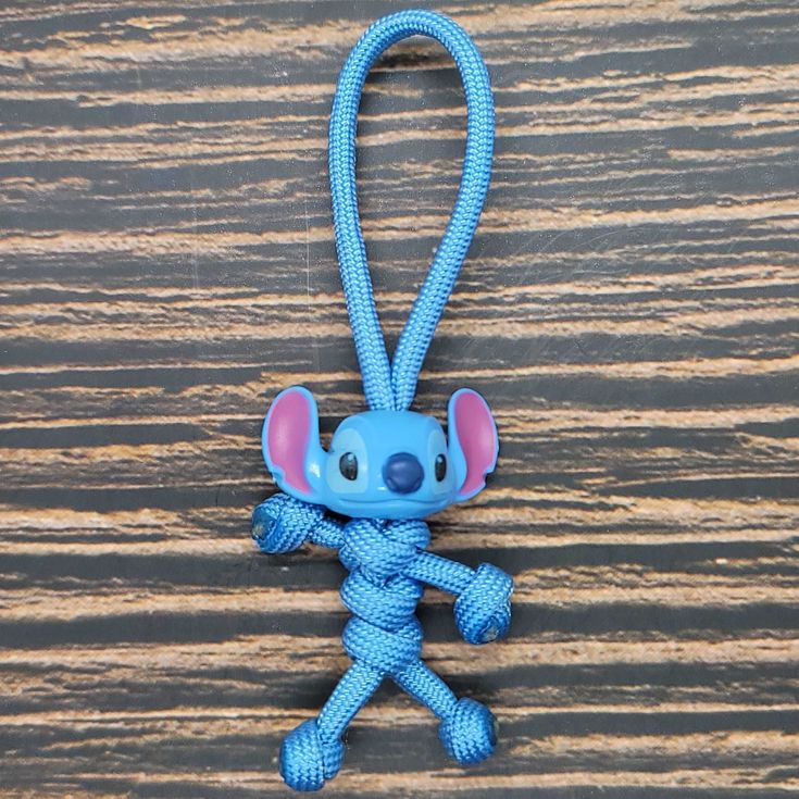 a blue keychain with a small cartoon character on it's side hanging from a wooden surface