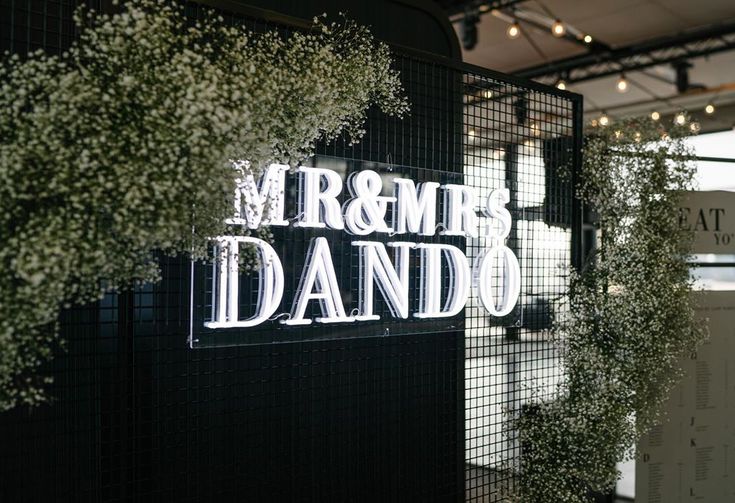 the sign for mr and mrs dando is lit up with white flowers in front of it