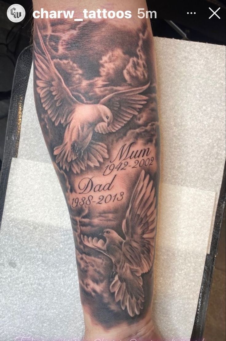 an arm tattoo with two birds on it and the words mum, dad and son written in