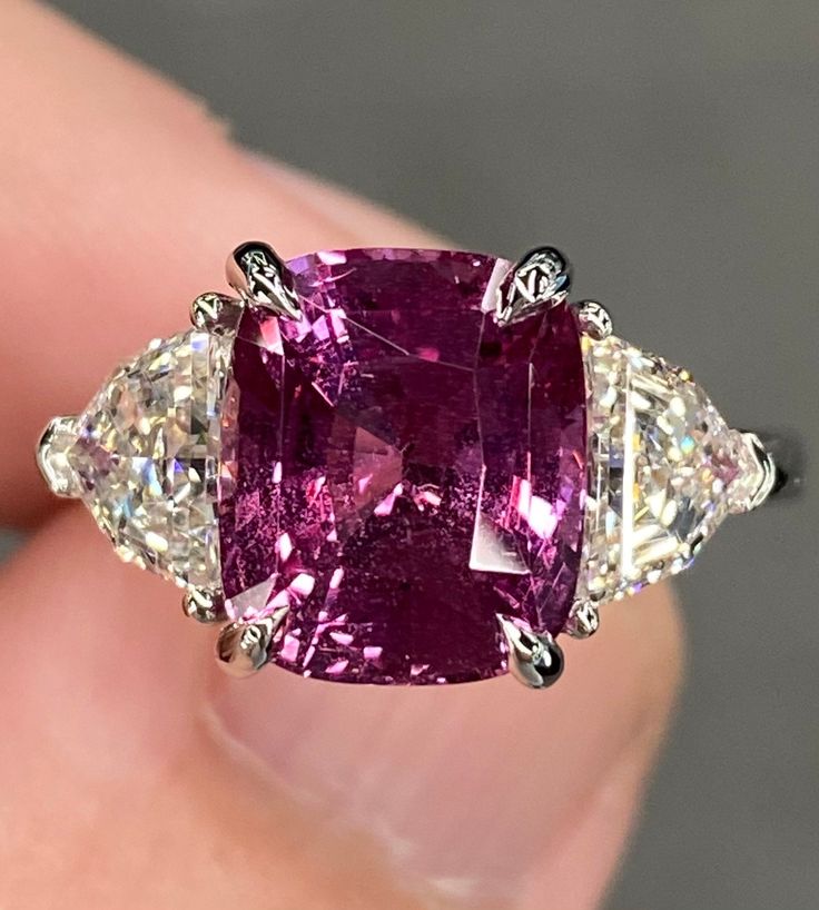 ALL THESE PHOTOS WERE TAKEN WITH AN ORDINARY IPHONE & HAVE NOT BEEN EDITED OR ENHANCED IN ANY WAY. The Center Stone is a Spectacular Natural GIA Certified 5.03 Ct Vivid Purplish Pink Cushion Cut Sapphire that measures approx 10.3 x 8.7 mm & was mined in Madagascar. It Checks all the boxes with phenomenal cutting, Beautiful Color, & amazing clarity.  The Mounting was 100% Custom Made Specifically for this Remarkable Sapphire out of Solid Platinum & is Stamped. It Features a matching pair of Natural Earth Mined G-H VVS-VS Epaulette Cut Diamonds that weigh 1.32 Ct Combined. They are both Very White (Near Colorless) Diamonds that are 100% clean to the eye as well as clean under 10x magnification. They are both Crystal Clear, Super Lively Diamonds that are Full of Brilliance, Fire, Spark & Flas Elongated Cushion Three Stone, Purple Diamond Engagement Ring, Diamond Platinum Ring, Pink Cushion, Elongated Cushion, Vvs Diamond, Purple Diamond, Platinum Diamond Rings, Colorless Diamond