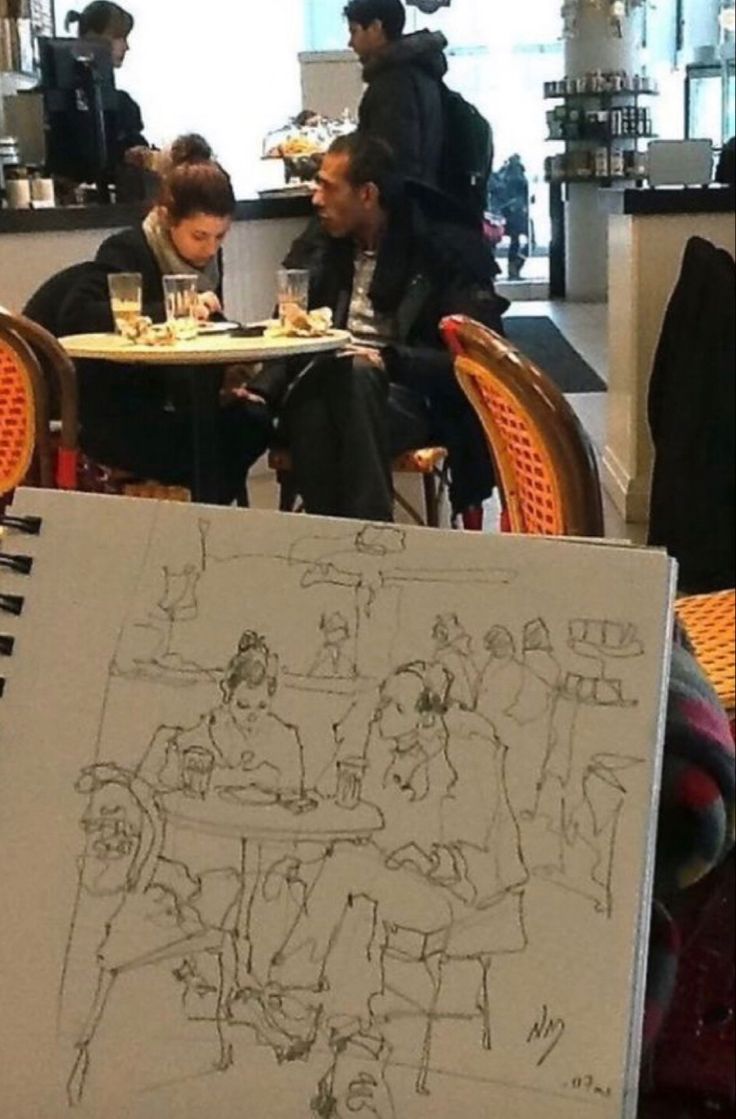 people sitting at tables in an open area with food on the table and one person drawing