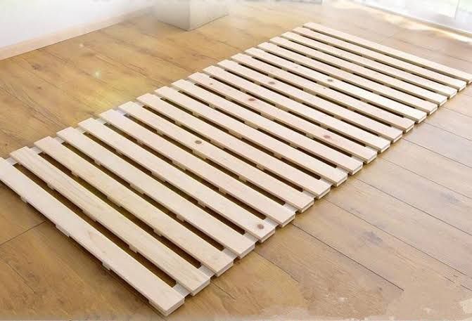 a wooden bed frame laying on the floor in front of a window with no curtains